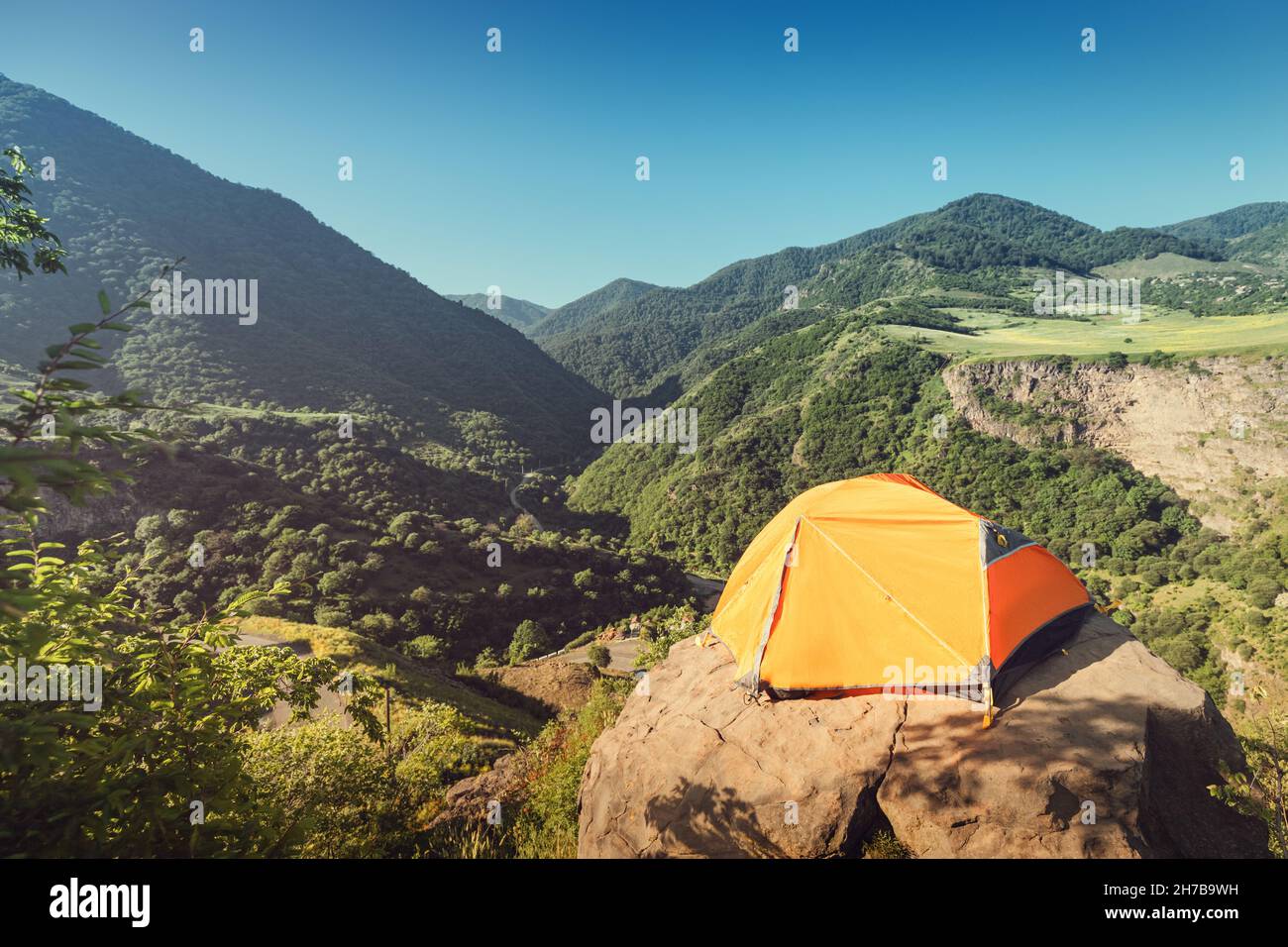 orange tent stands on a cliff on the edge of a high cliff into a mountain gorge. Dangerous camp of rock climbers and mountaineers in Transcaucasia Stock Photo