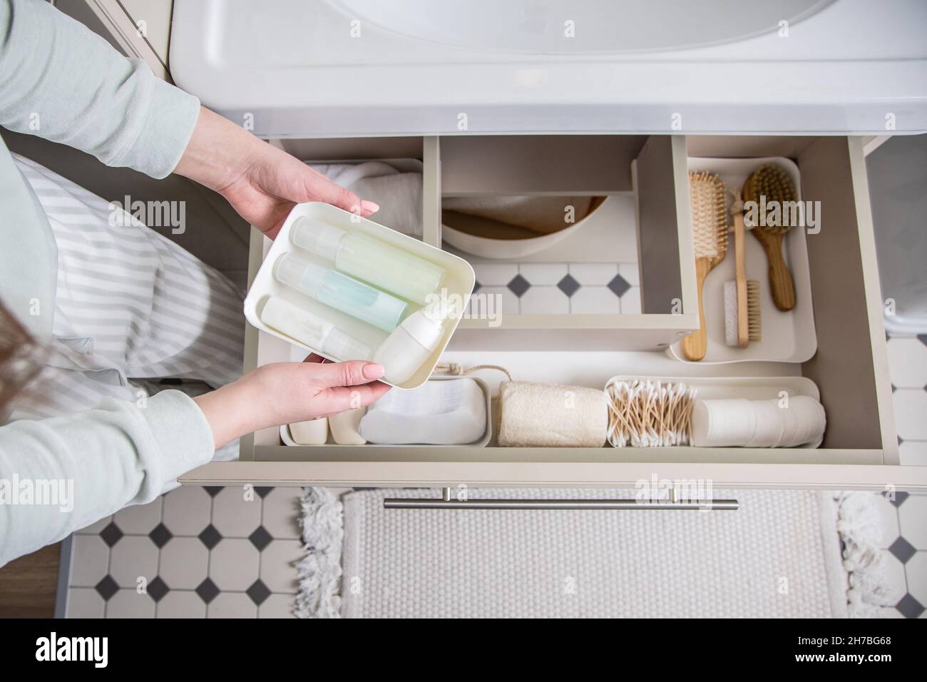 Housewife hands putting rolled up towel into drawer under sink