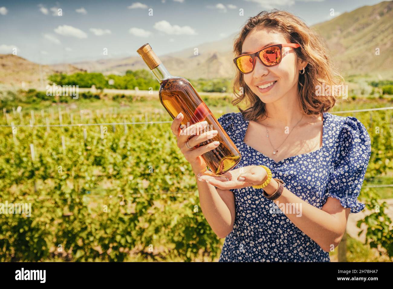 Woman with a bottle of grappa or cognac on the background of a vineyard in the mountains. The concept of strong alcohol from the highest grape varieti Stock Photo