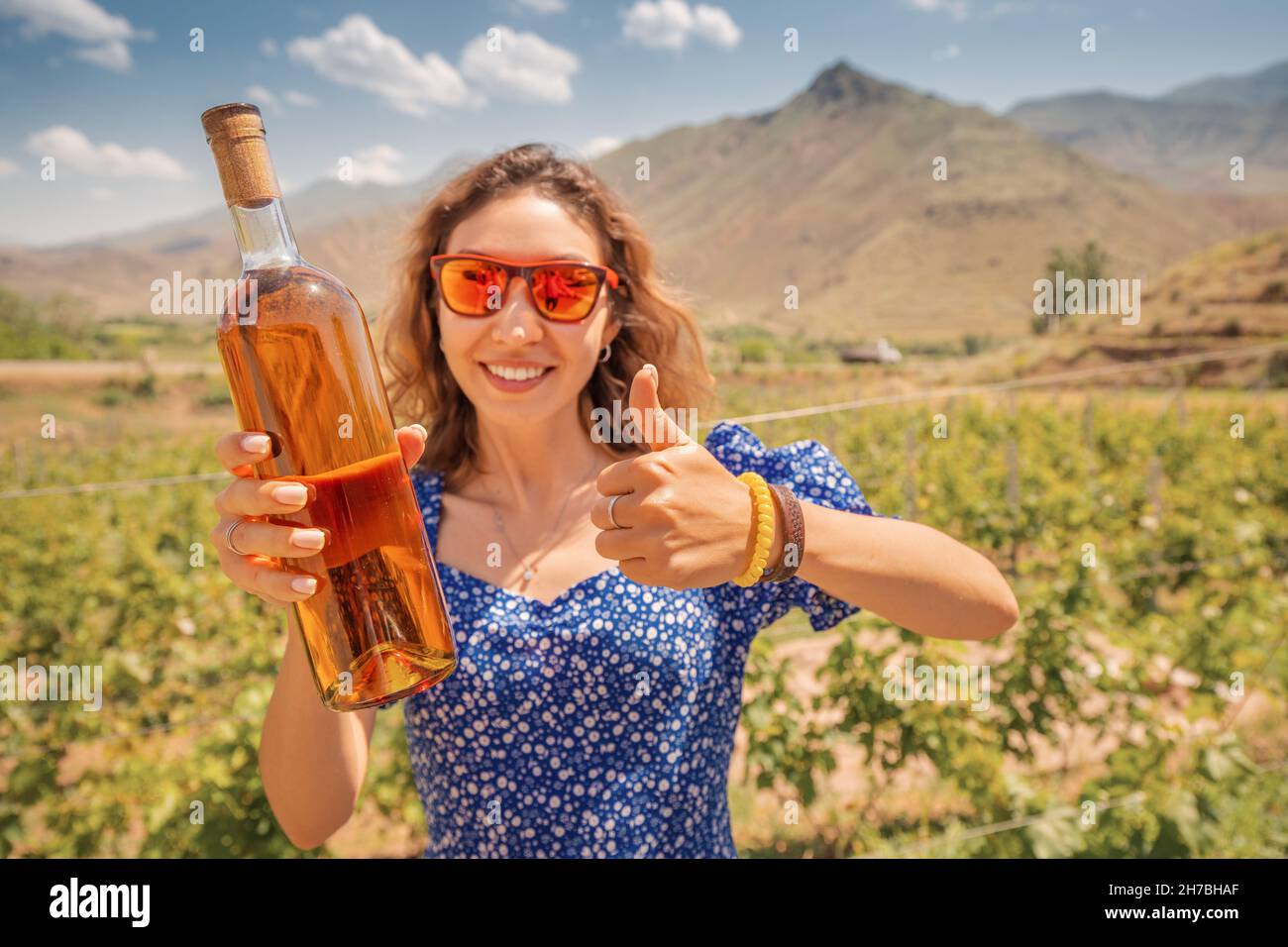 Happy woman with a bottle of grappa or cognac on the background of a vineyard. Strong alcohol spirits from the richest grape varieties Stock Photo