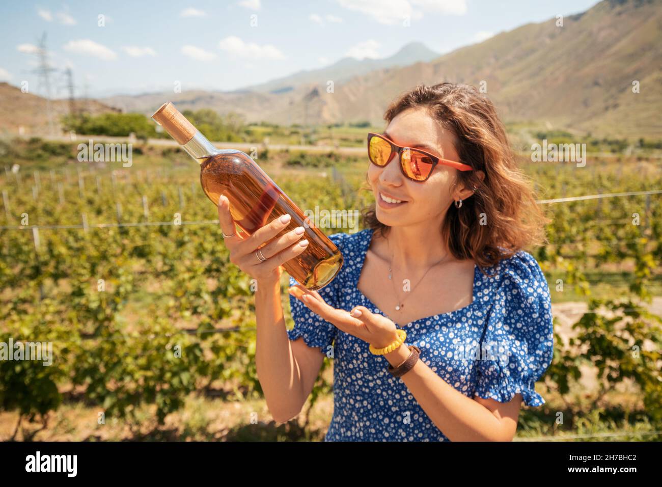 Woman with a bottle of grappa or cognac on the background of a vineyard in the mountains. The concept of strong alcohol from the highest grape varieti Stock Photo