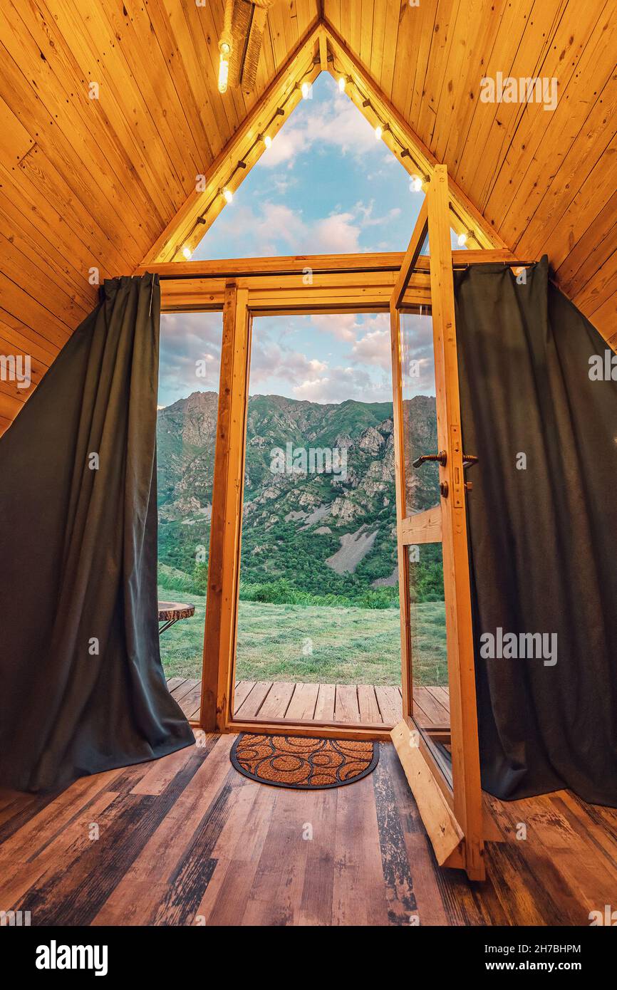 view from a small wooden chalet house in the mountains outside through a glass door and window. The concept of glamping and idyllic holidays Stock Photo