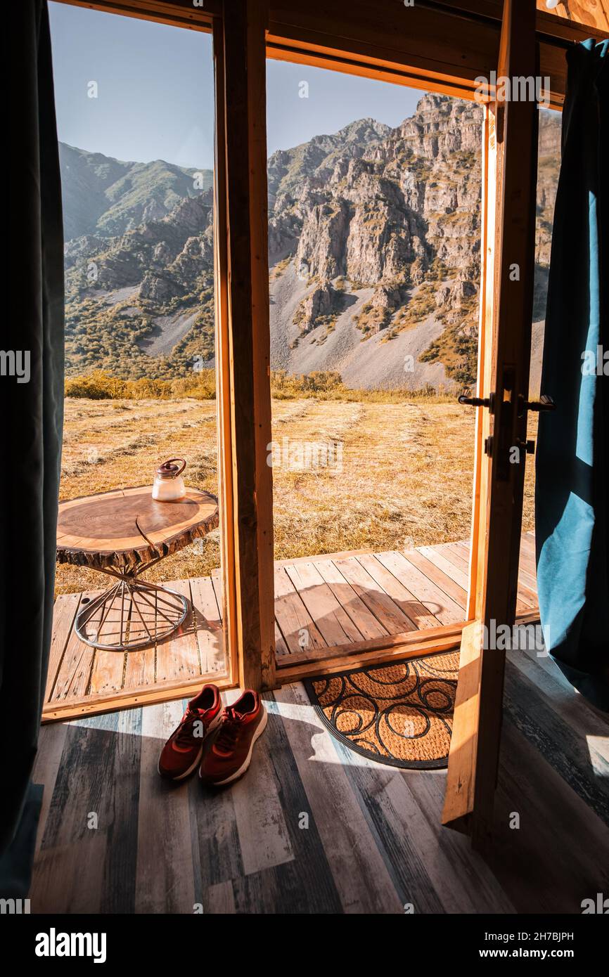 view from a small wooden chalet house in the mountains outside through a glass door and window. The concept of glamping and idyllic holidays Stock Photo