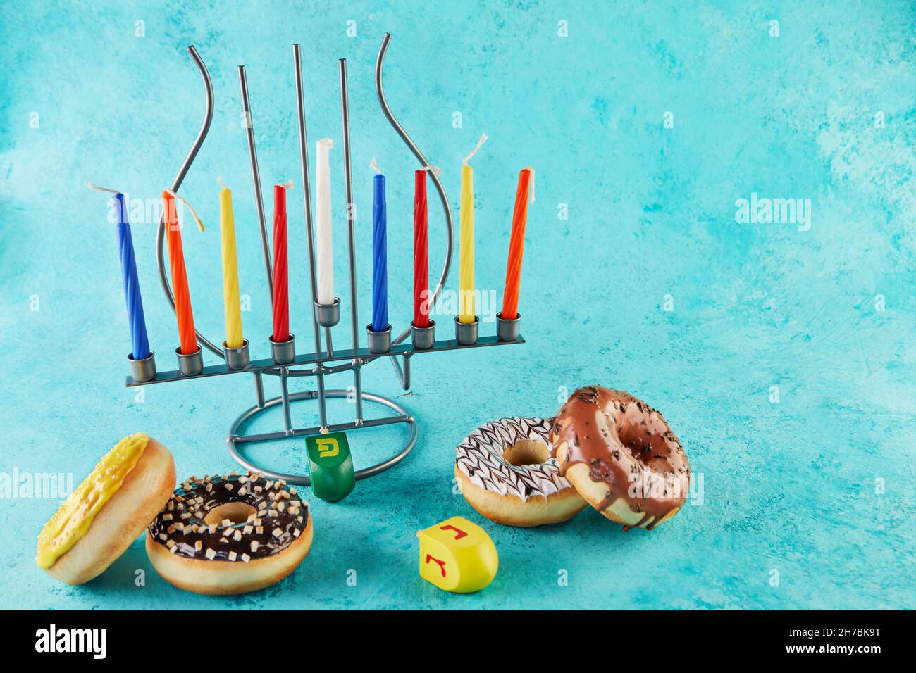 Happy Hanukkah and Hanukkah Sameach - traditional Jewish candlestick with candles, donuts and spinning tops on blue background. Inscription in Hebrew Stock Photo