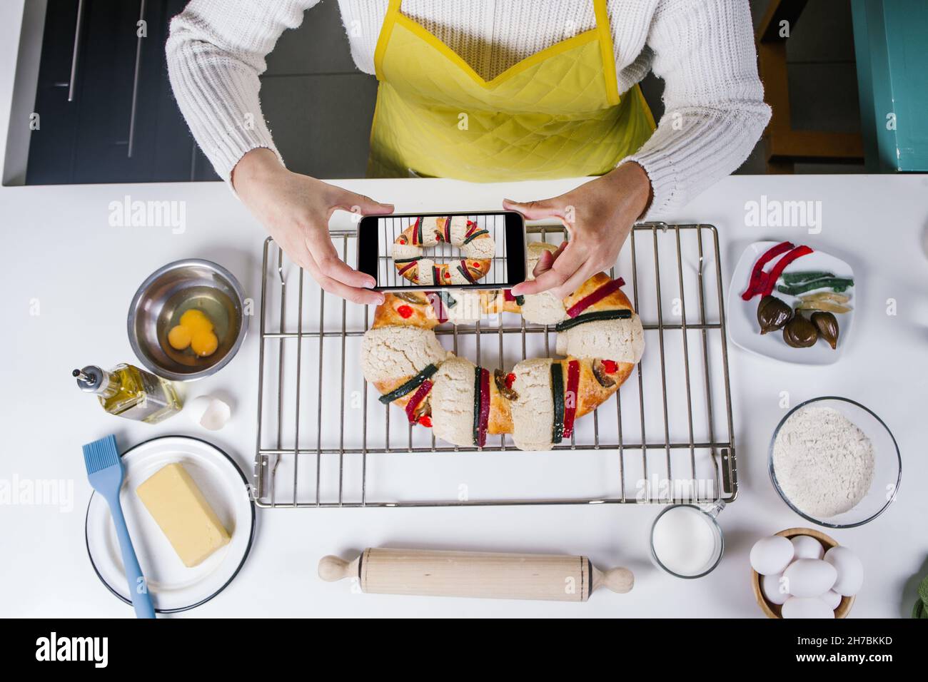 mexican woman baking a traditional rosca de reyes or epiphany cake and taking photo with mobile phone in kitchen at home for Kings Day in Mexico Latin Stock Photo