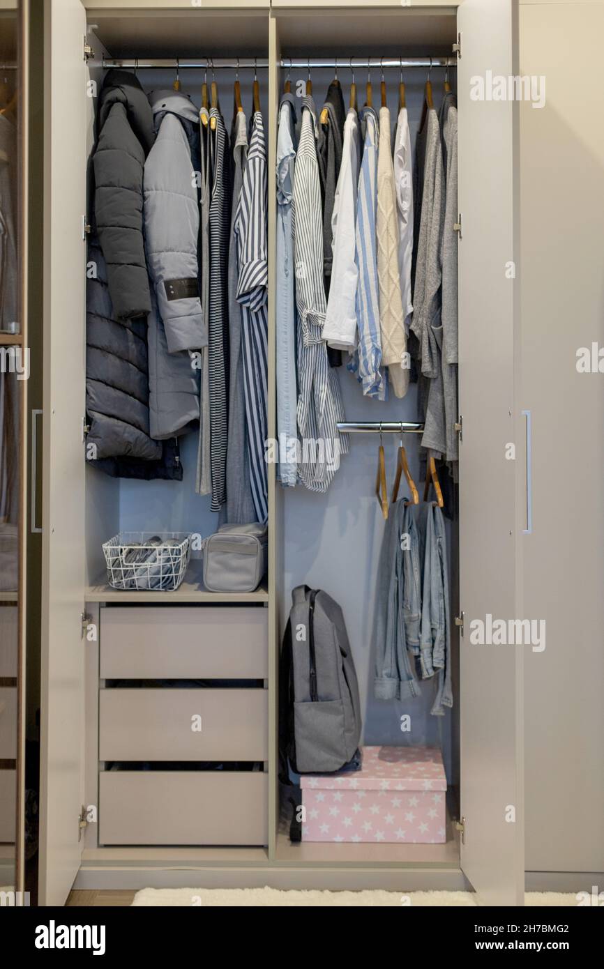 Wardrobe with perfect order clothes in blue and light shades on the hangers and things in containers. Stock Photo