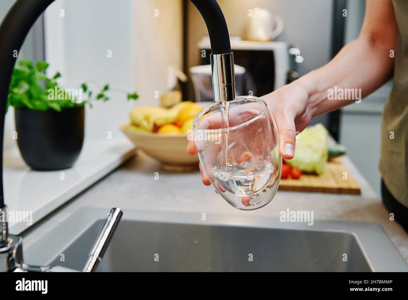 Woman pouring water from faucet into glass at the kitchen Stock Photo