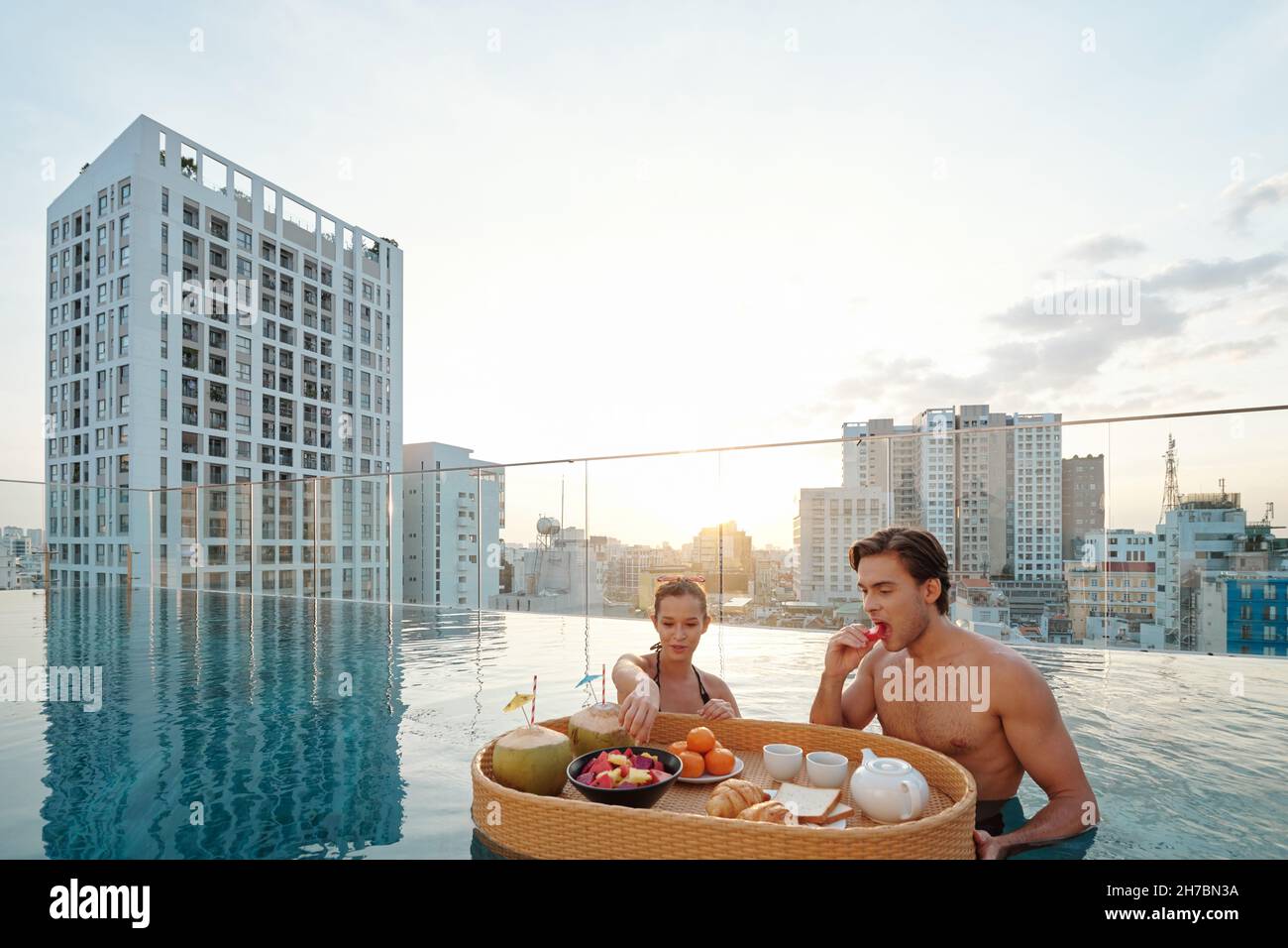 Eating In The Pool Attractive young man and woman eating delicious breakfast in rooftop ...