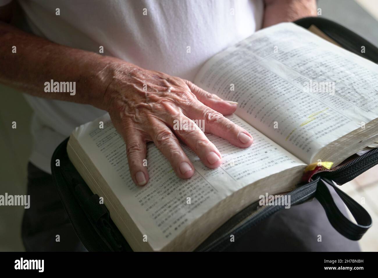 Wrinkled hand of senior man on top of an open bible. Stock Photo