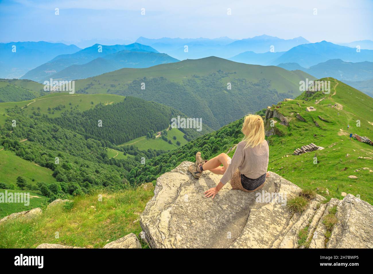 Tourist woman on a rock on top view of Monte Generoso or Calvagione Swiss mount. Aerial skyline of Lugano lake of Ticino canton. Top of cog train Stock Photo