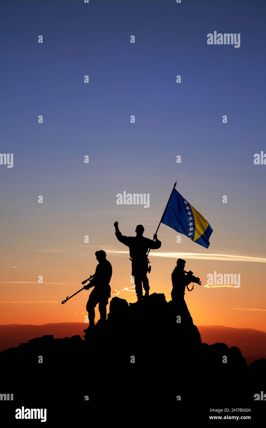 Three unrecognizable armed soldiers with the Bosnian flag on the top of the mountain Stock Photo