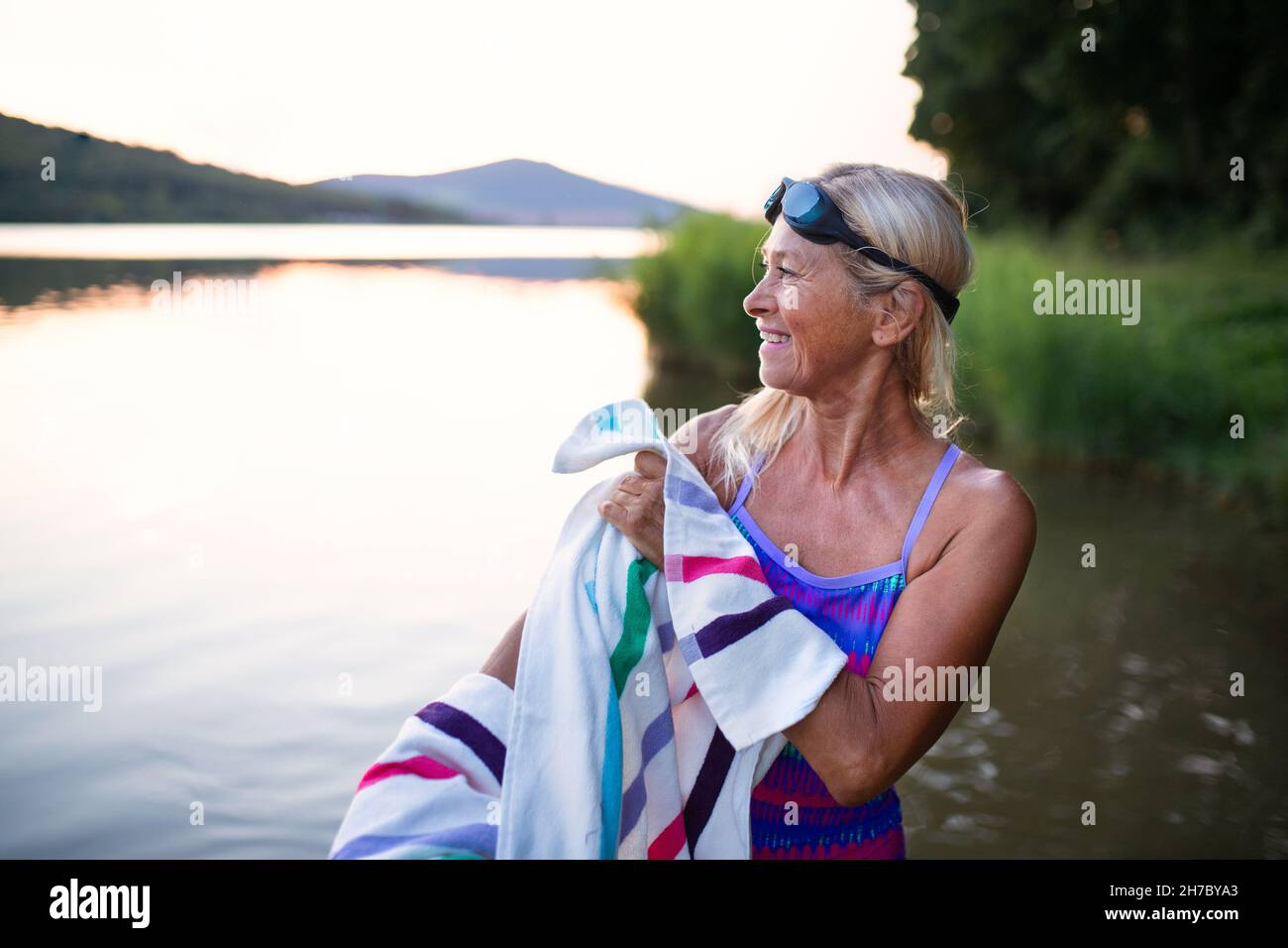 Portrait of active senior woman swimmerdrying herself with towell outdoors by lake. Stock Photo