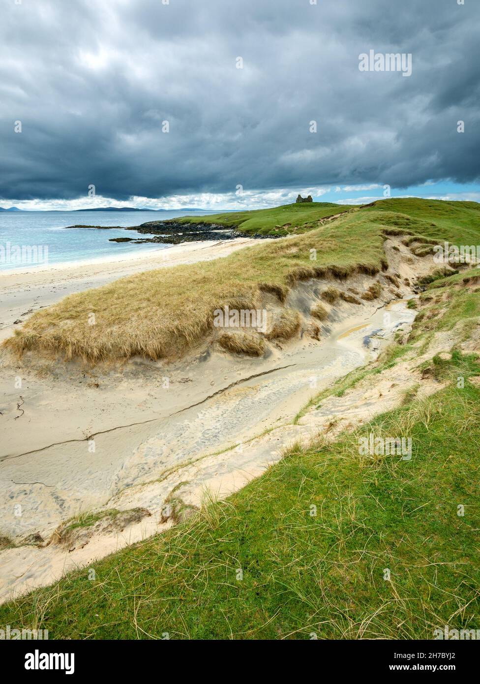 Dark skies over sand dunes with the ruins of Toe Head Chapel ( Rudh an Teampuill ) on a distance headland, Gob An Tobha, Isle of Harris, Scotland, UK Stock Photo