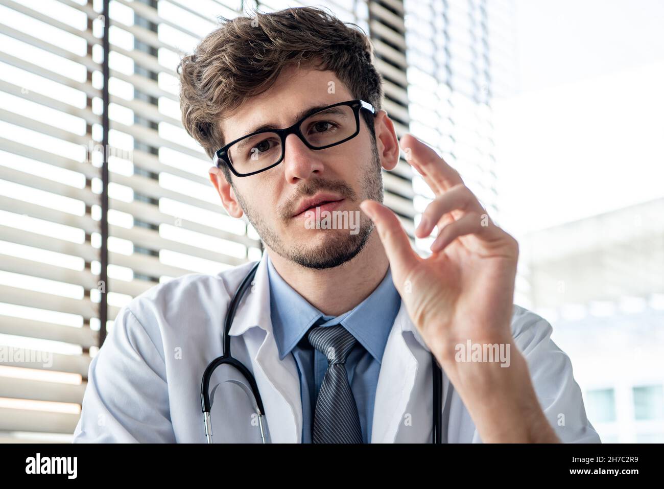 Young male doctor looking at camera and explaining, distance medical consultation service or telehealth concepts Stock Photo
