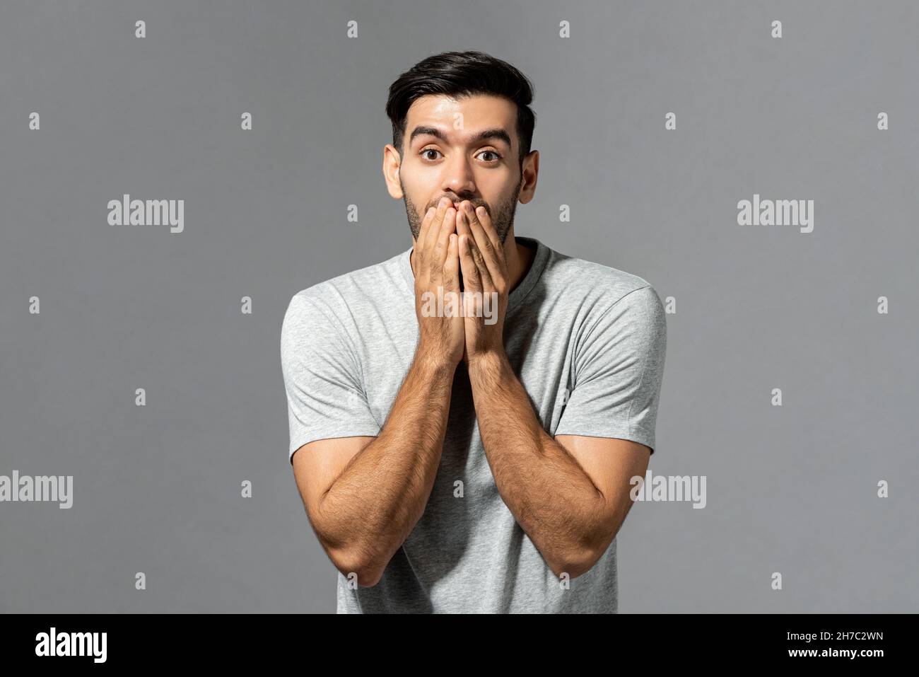 Shocked surprising young Caucasian man with hands covering mouth in isolated light gray studio background Stock Photo