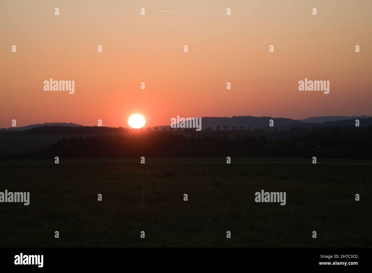 romantic sunset behind a hill in front of a meadow. Tuscan view with the row of trees in the background Stock Photo