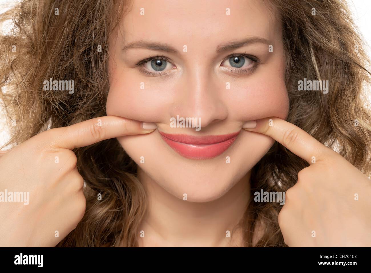 a young beautiful blonde forcing her smile with her fingers on a white background Stock Photo