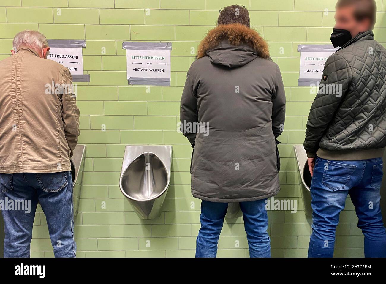 Munich, Deutschland. 22nd Nov, 2021. Topic picture Corona hygiene measures-distance in the men's room-breaking the corona rule. Every second urinal, urinal, urinal, toilet is blocked and out of order in order to comply with the distance rule, which one of the three men does not follow. Credit: dpa/Alamy Live News Stock Photo