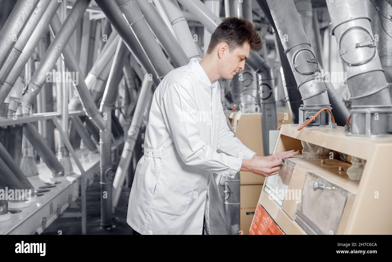Operator checks quality of finished food products wheat flour. Modern electrical mill machinery