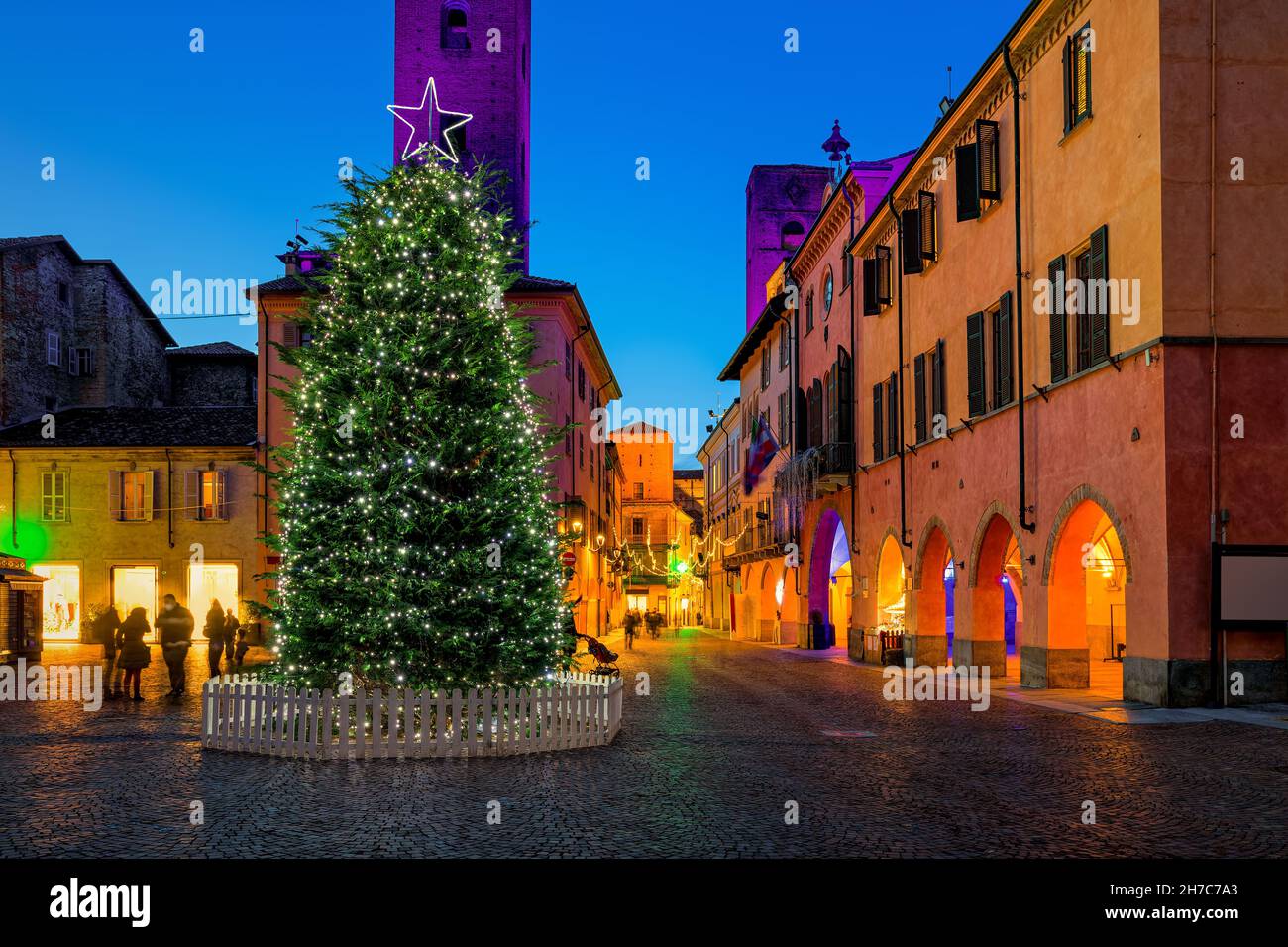 Illuminated Christmas tree on town square in the evening among historic houses in Alba, Piedmont, Northern Italy.. Stock Photo
