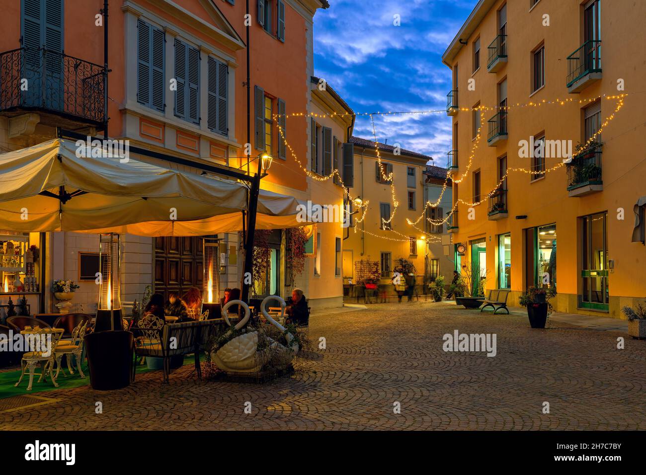 Outdoor restaurant on small cobblestone town square illuminated with Christmas lights in the evening in Alba, Piedmont, Northern Italy. Stock Photo
