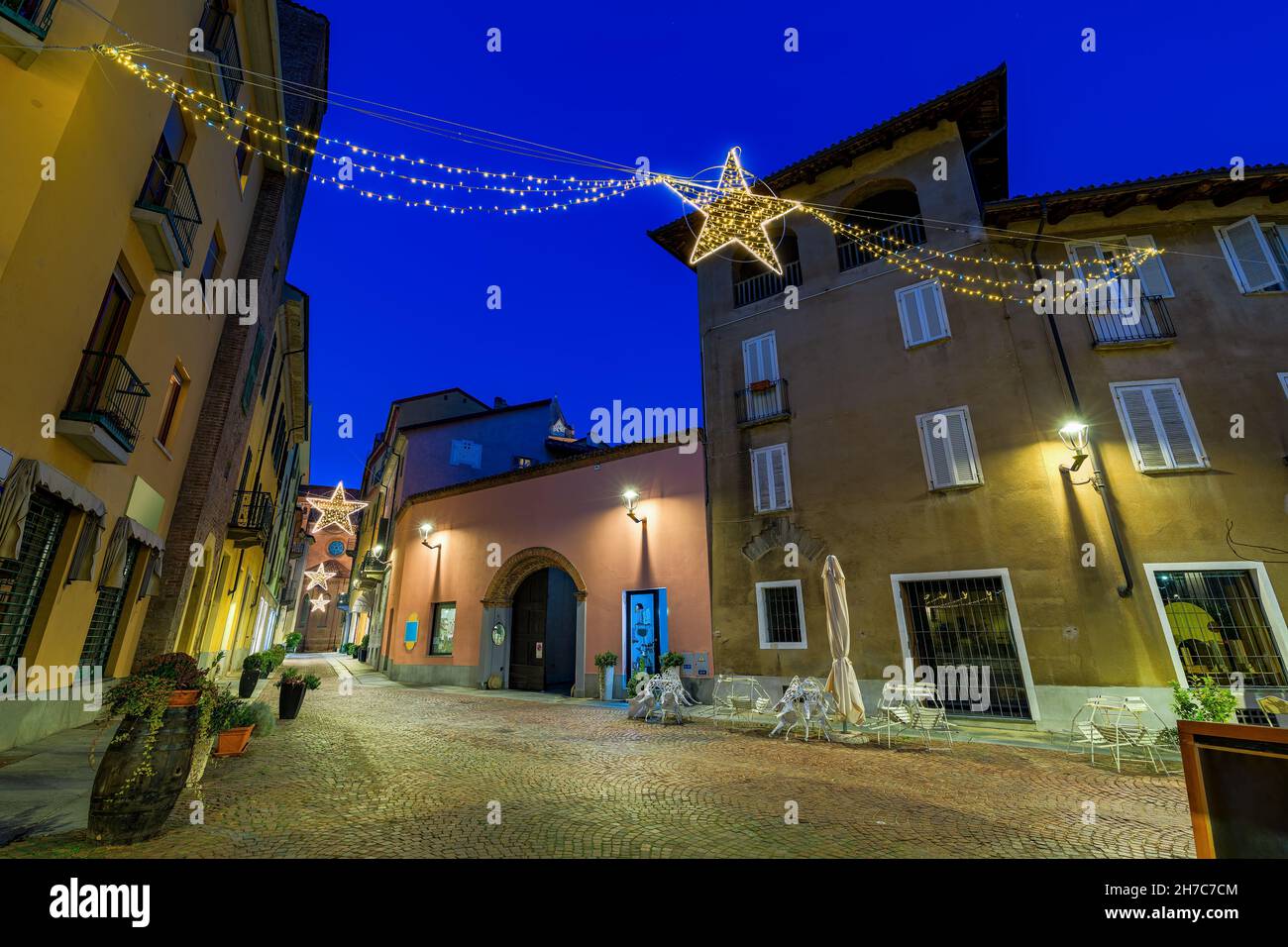Christmas illumination over small cobblestone town square and historic buildings in the evening in Alba, Piedmont, Northern Italy.. Stock Photo