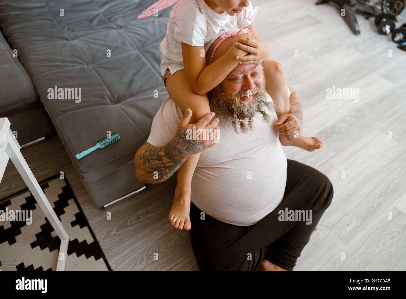 Daughter sits on shoulders of positive plump father in living room Stock Photo