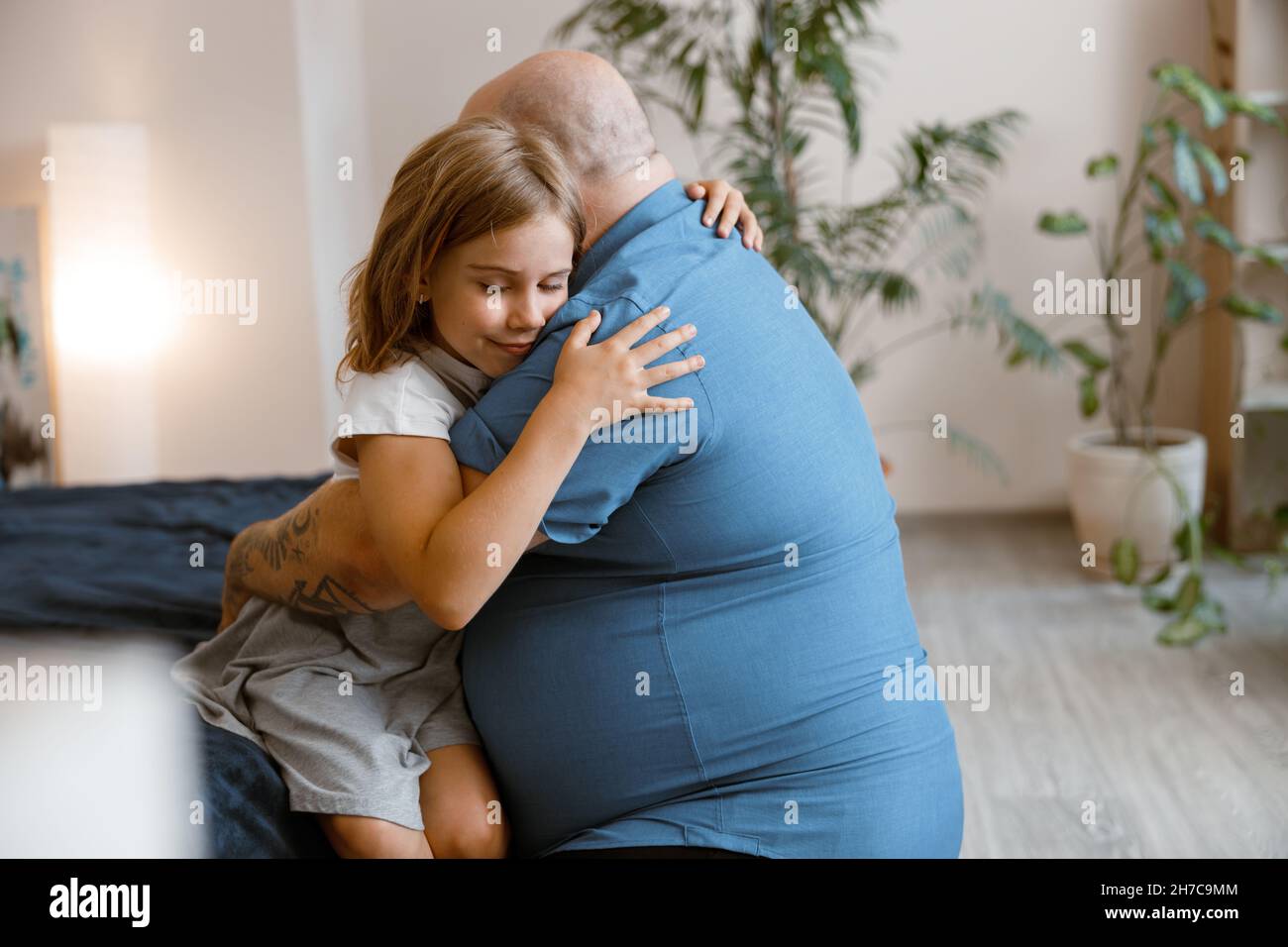 Happy little girl and obese daddy hug sitting on bed in light room Stock Photo