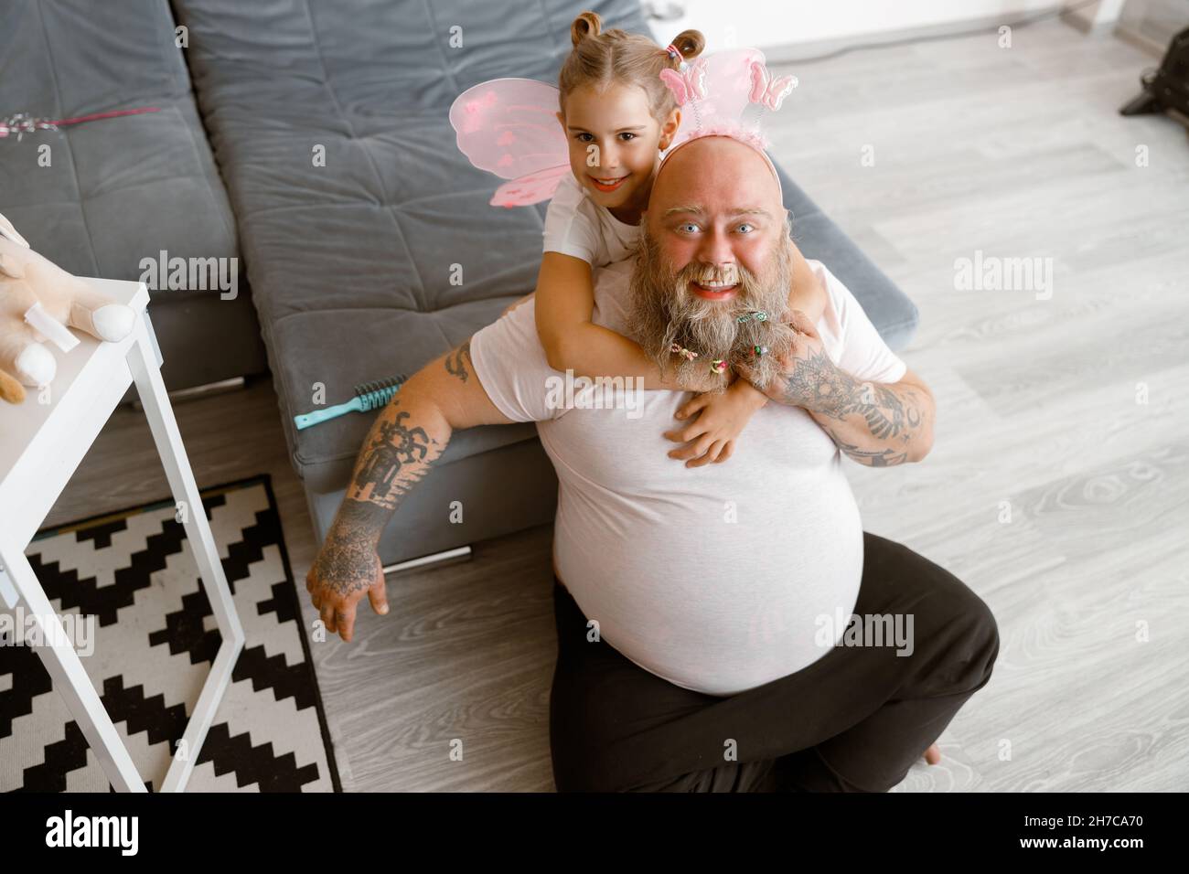 Happy little girl hugs funny obese daddy sitting on floor in living room Stock Photo