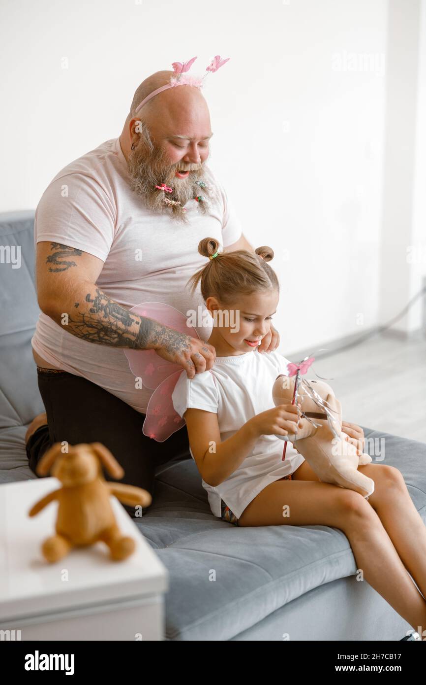 Funny daddy does massage to little girl holding toy dog and magic stick in living room Stock Photo