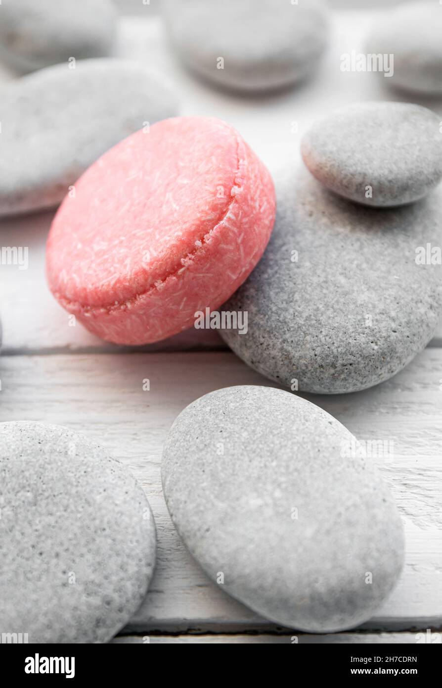 Pink color solid shampoo, conditioner bar on flat sea stones. Minimalist beauty set indoors. Shallow depth of field. Stock Photo
