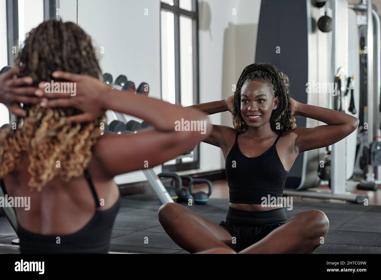 Beautiful smiling young sportswoman doing exercises in front of mirror ...