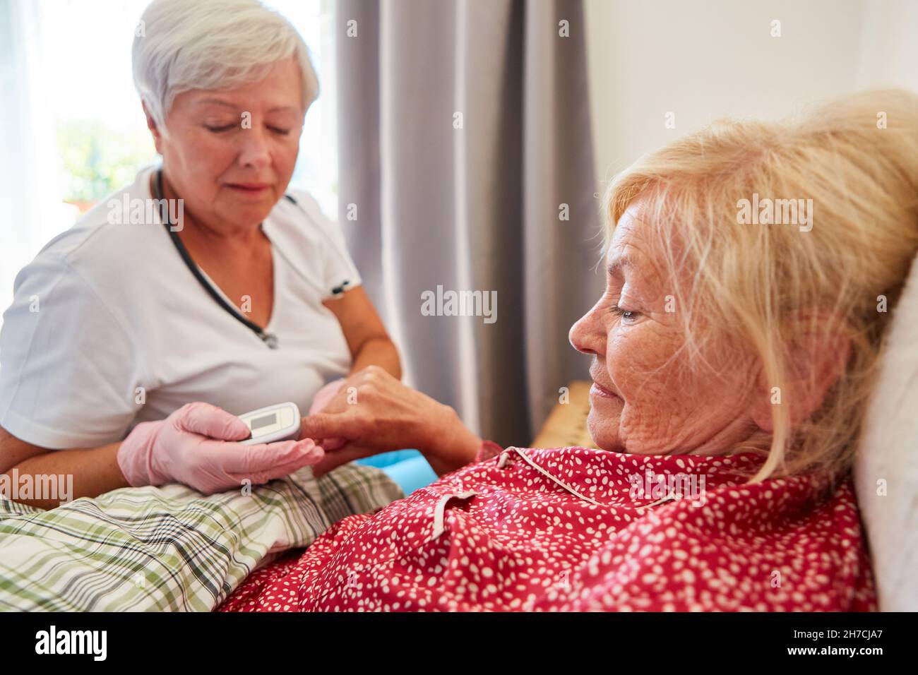 Geriatric nurse measures heart rate of sick elderly woman at home in bed with the pulse oximeter Stock Photo