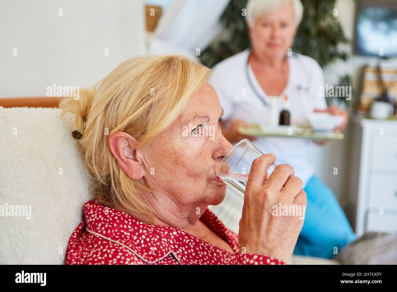 Sick elderly woman takes medication with a glass of water in home care Stock Photo