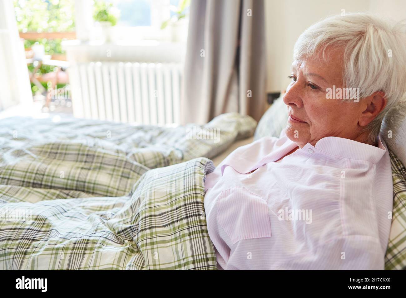 Sick old woman in bed as a thoughtful patient at home or in the