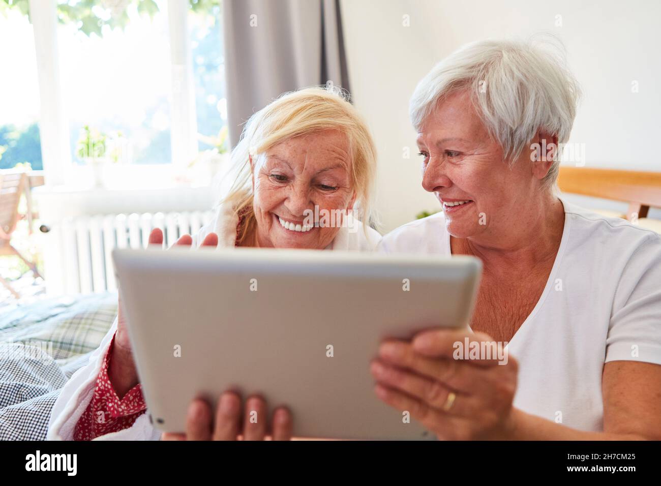 Two seniors have fun on the tablet computer while video chatting on social media at home Stock Photo