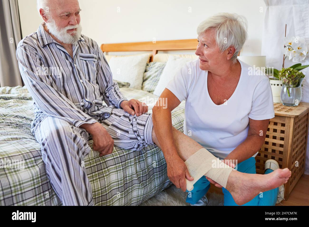 Carer applies a bandage to sick senior man after a broken tibia at home Stock Photo