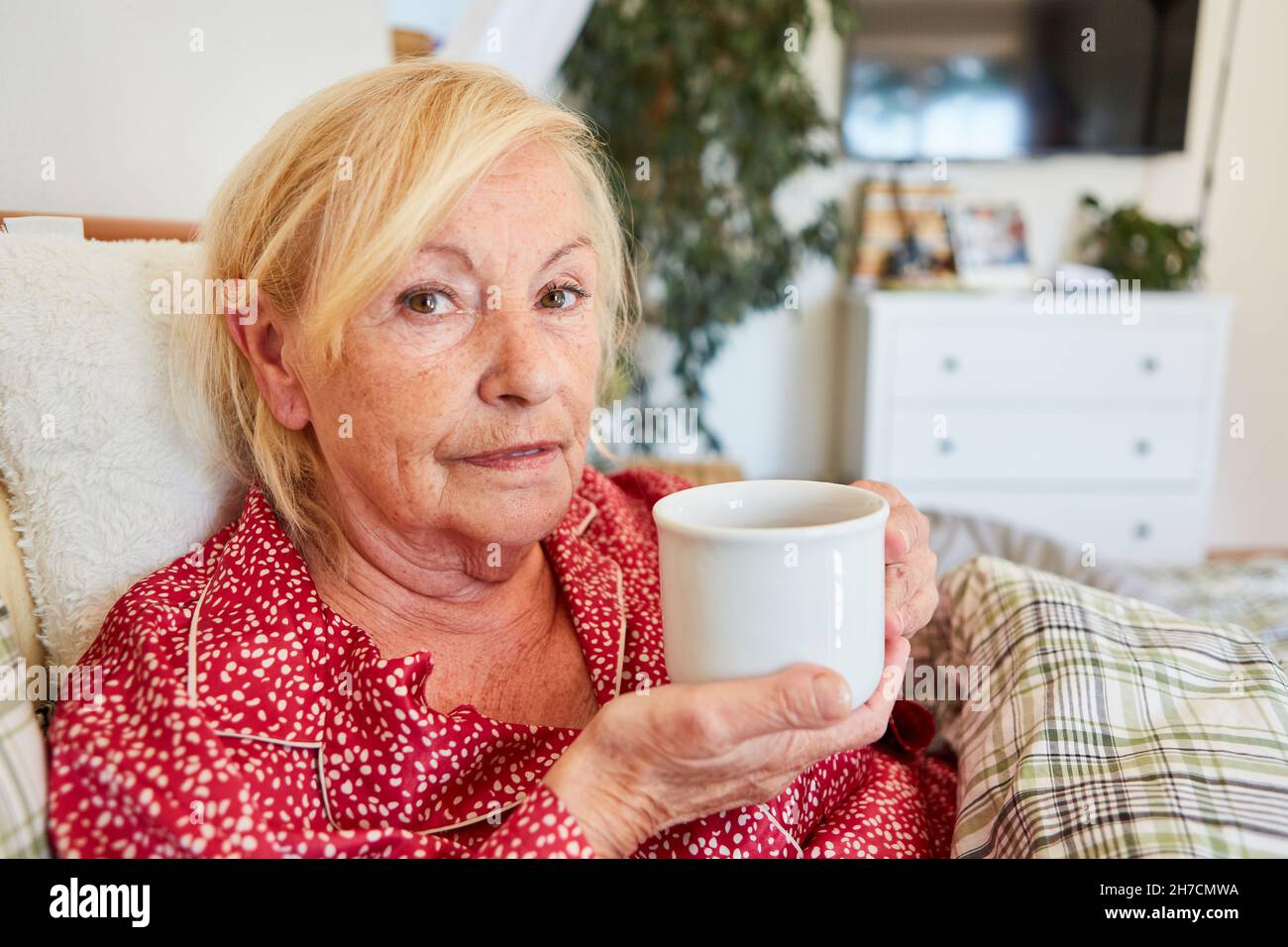 Elderly sad woman drinking coffee in bed at home or retirement home Stock Photo