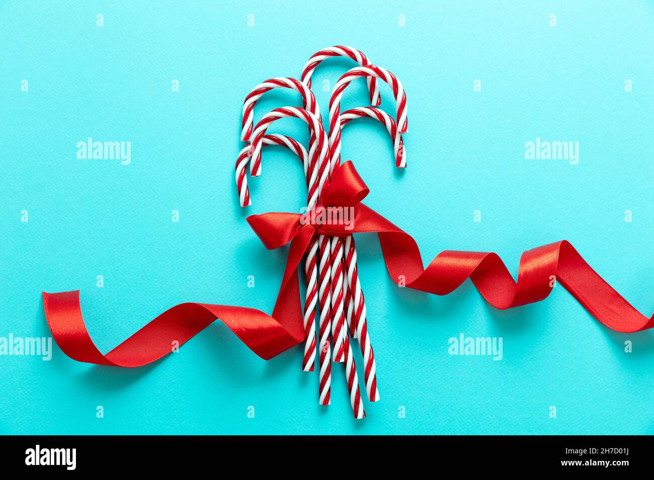 Candy canes bunch on blue background. Christmas peppermint red white candies with red ribbon bow. Merry Xmas greeting card template Stock Photo