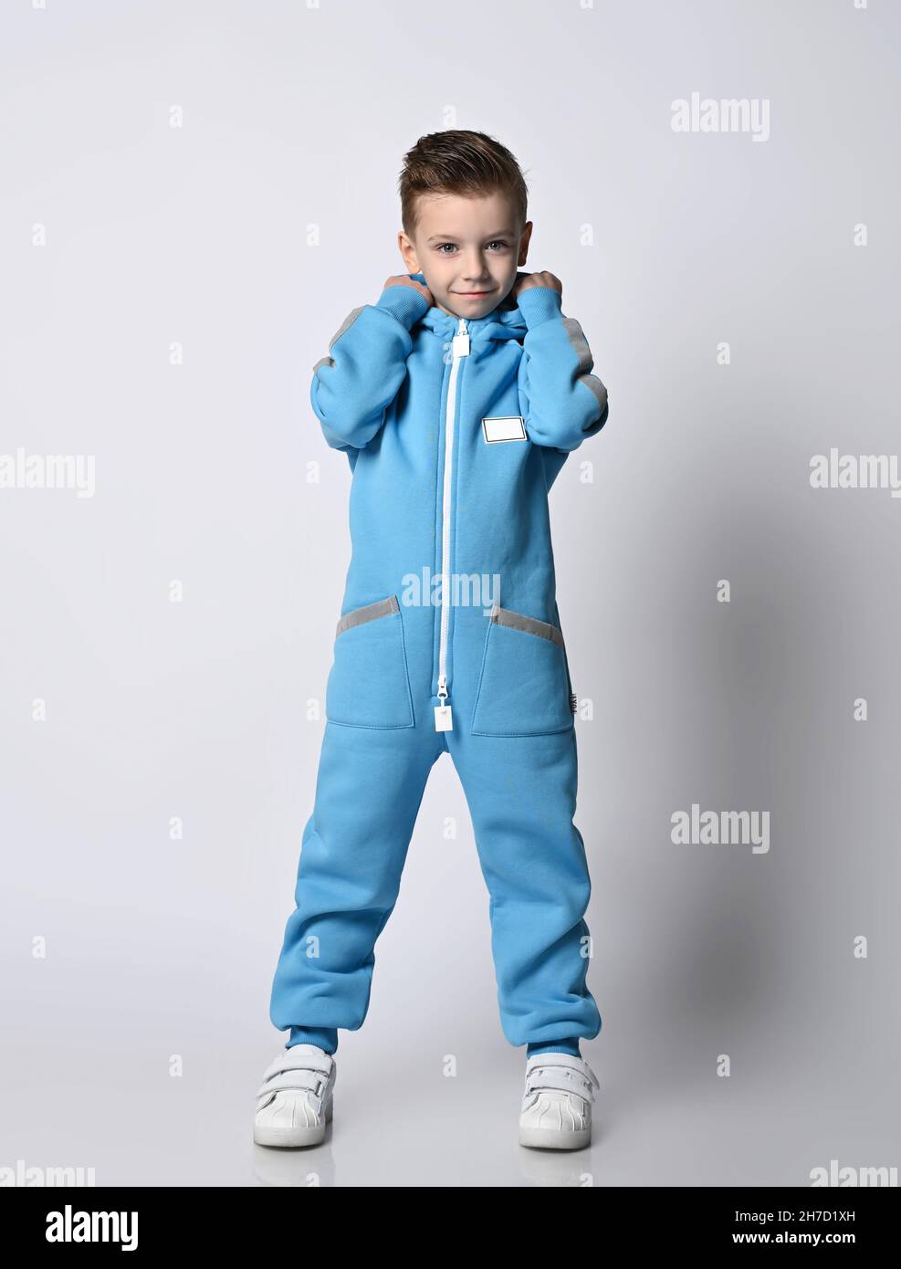 Smiling kid boy in blue jumpsuit with zipper and reflective stripes stands  holding his cowl with hands, putting on hood Stock Photo - Alamy