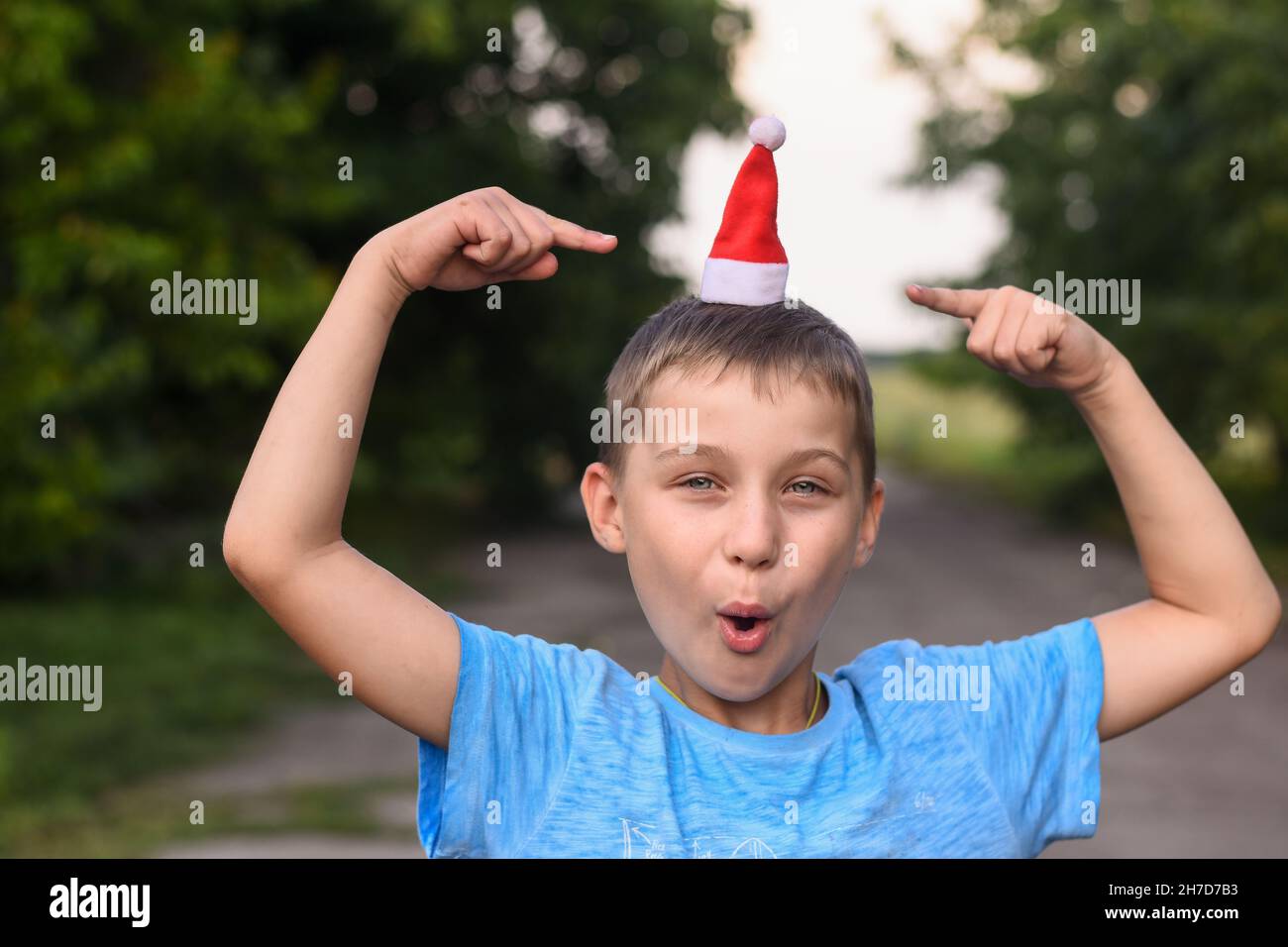 boy jokes, puts a small Santa hat on his head and points at it with his index fingers Stock