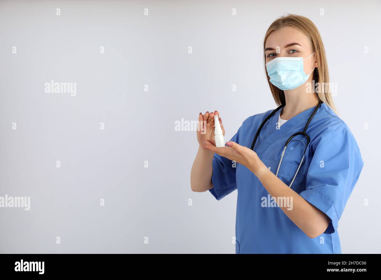 Young nurse with nasal spray on light background, seasonal cold