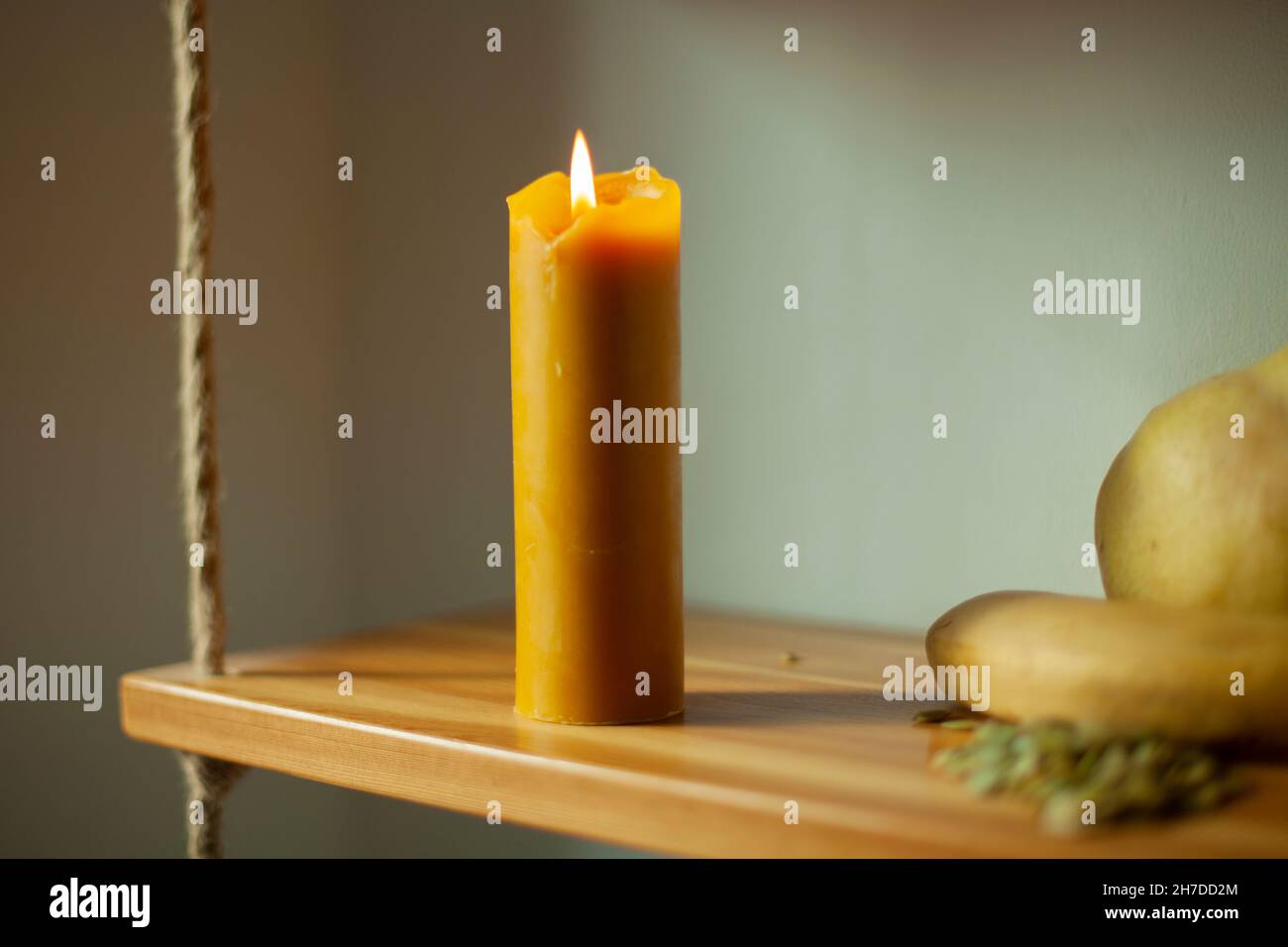 The candle burns during the day. A wax candle is on a shelf. Flame from