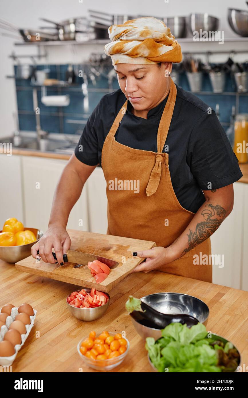 Vertical waist up portrait of tattooed woman cutting vegetables while ...
