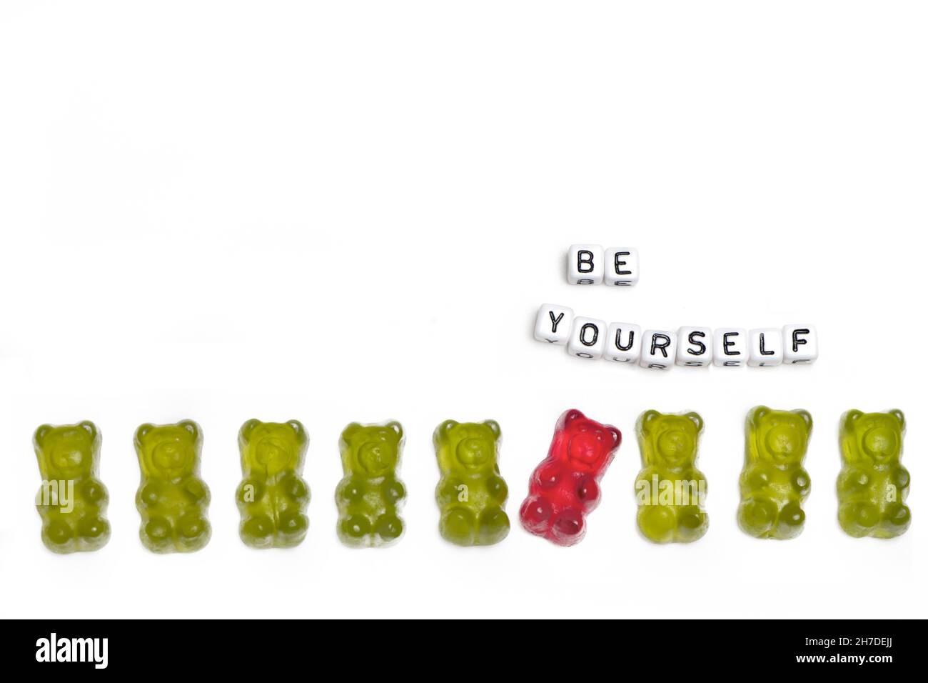 a row of green gummy bears in which a red guy behaves differently out of a concept for individuality and being different is isolated on a white backgr Stock Photo