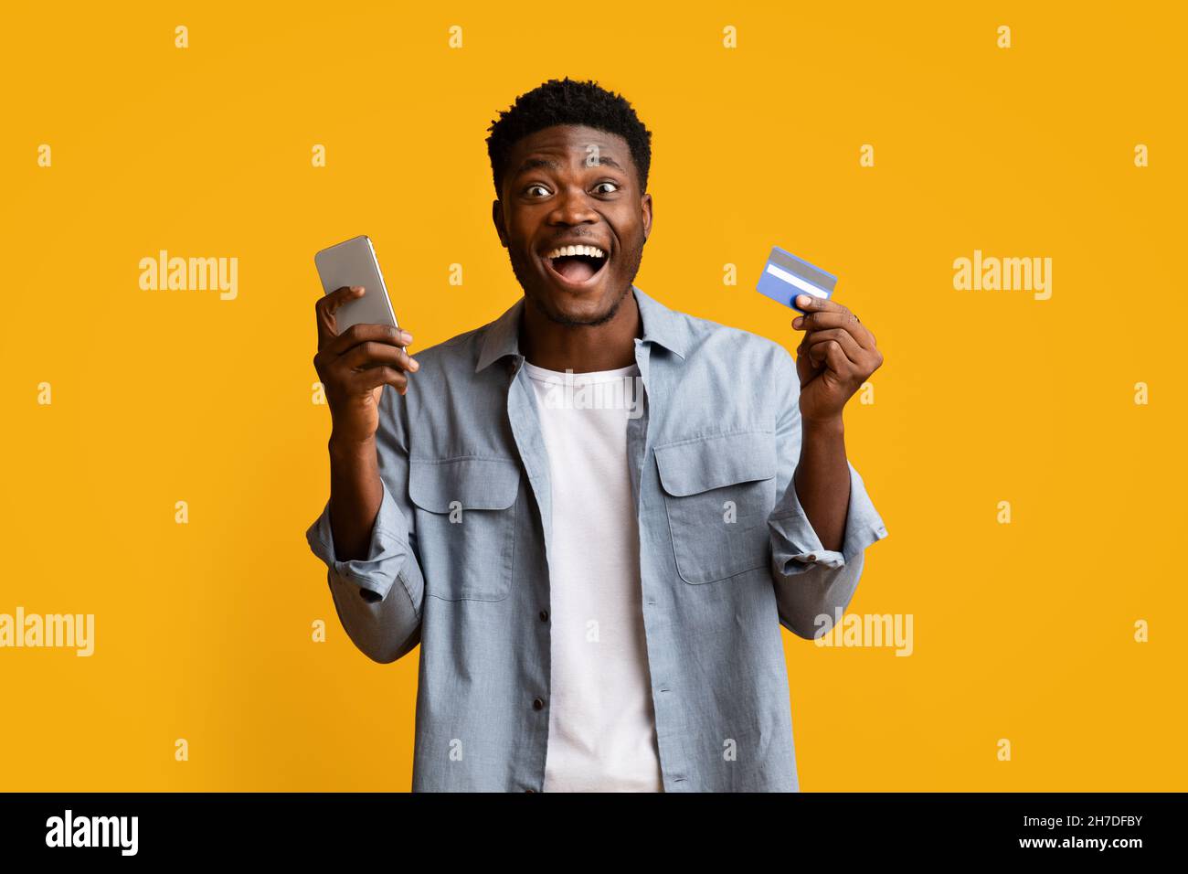 Emotional black guy holding smartphone and credit card Stock Photo - Alamy