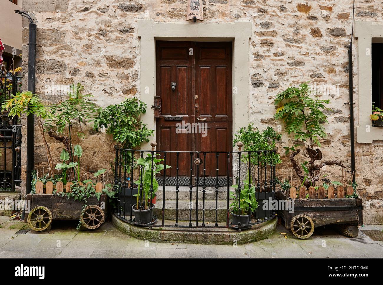 main entrance with wooden door, iron fence and wooden carts with plants on the sides Stock Photo