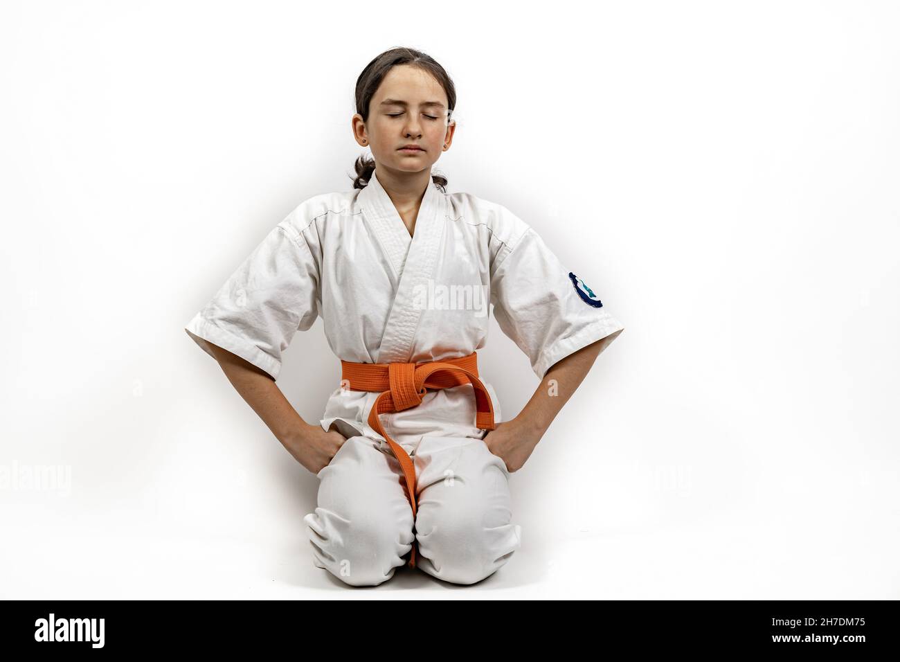 Karate girl on a white background. A sportive Caucasian brunette in a white kimono is engaged in martial arts. She meditates in the seiza position wit Stock Photo