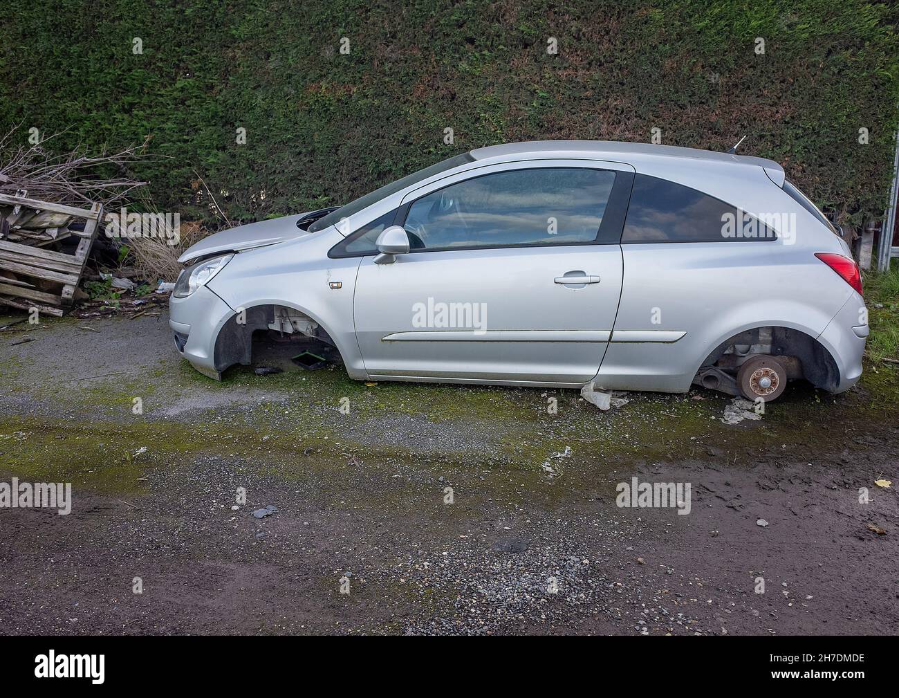 Abandoned small silver car with no wheels left of waste ground. Stock Photo