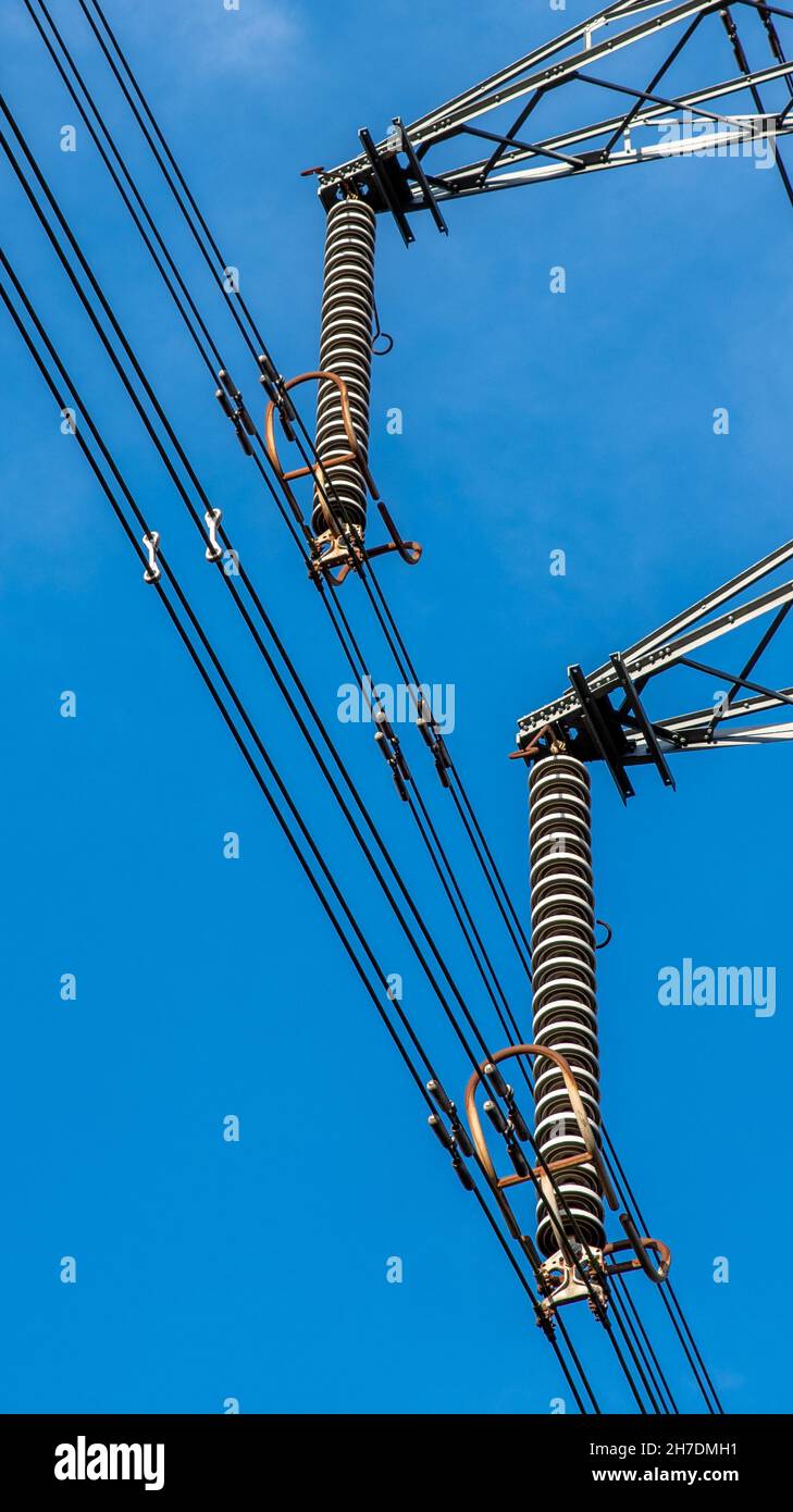 Two electrical insulators with power cables on a pylon with blue sky background. Stock Photo